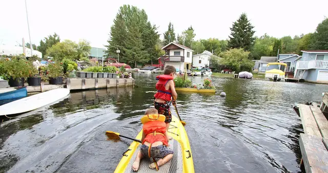 Kids paddleboarding in the canal among cottages